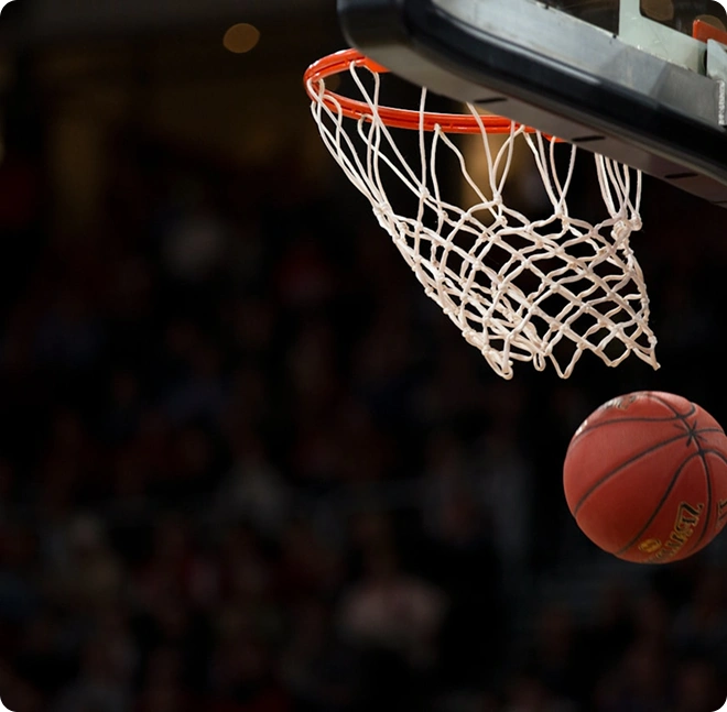 Close-up de uma bola de basquetebol a aproximar-se do cesto e da rede durante um momento emocionante do jogo.