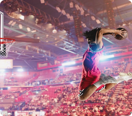 Jogador profissional de basquetebol a realizar uma enterrada poderosa numa arena interior cheia, sob luzes intensas do estádio.